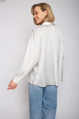Emily Bluse 102 offwhite: Frau trägt eine weiße, oversized Hemdbluse mit überschnittener Schulter und Knopfblende. Die Bluse aus leicht fließendem Viskose Satin hat eine Falte im Rückenteil.