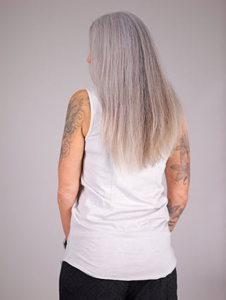 Frau mit Tattoos trägt das Cotton Candy Top Heidelore in Grau, zeigt dessen Rundhalsausschnitt und breite Träger aus Baumwolle-Elastan-Mix. Rücken- und Arm-Tattoos sichtbar.