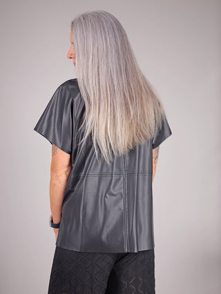 Eine Frau trägt das MAT Fake Leder Shirt 1074 in Schwarz, ein kurzärmeliges Shirt mit Rundhalsausschnitt, das aus 94% Polyester und 6% Elastan besteht.