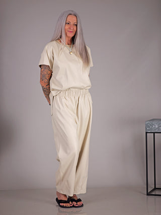 Frau mit Tätowierungen trägt MAT Hose 2074 creme, eine bequeme Fake-Leder-Culotte aus Viskose, während sie in einem Innenraum steht.