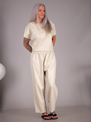 MAT Hose 2074 creme: Eine Frau trägt eine cremefarbene Fake-Leder-Culotte mit Gummibund. Sichtbar sind schwarze Sandalen und tätowierter Arm. Die Culotte fällt normal aus und betont Komfort und Stil.