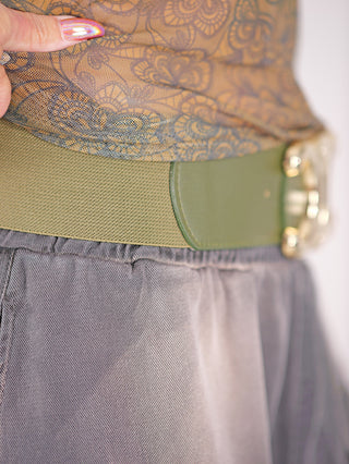 Person trägt Gürtel CC Groß grün, ein hochwertiger, elastischer Taillengürtel mit goldfarbener Schließe, ideal zum Abrunden von Outfits.