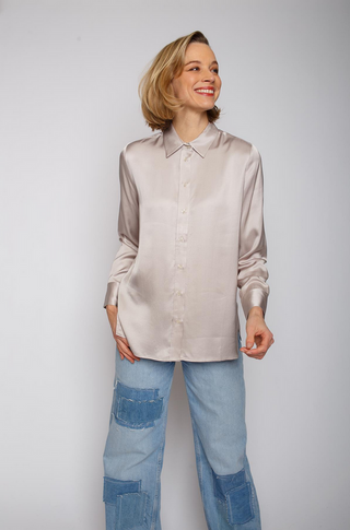 Emily Bluse 705 taupe: Frau trägt eine beige Hemdbluse mit durchgehender Knopfleiste und langen Ärmeln, kombiniert mit einer Jeans mit Patchwork-Details. Bluse aus leicht fließendem Viskose-Satin.