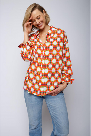 Emily Bluse 890 multi/geo: Frau in farbenfroher Hemdbluse mit grafischem Druck, lässiger Passform und überschnittener Schulter, berührt lächelnd ihr Haar.