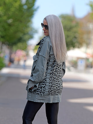 Eine Frau trägt die coole, Leopardenprint OFF#DLY Jacke Celia khaki mit offenen Kanten und großen Brusttaschen, kombiniert mit Sonnenbrille und modischem Street-Style.