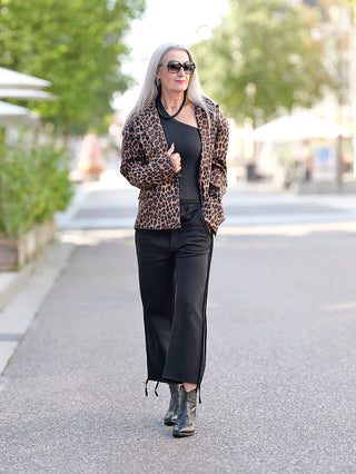Frau trägt den OFF#DLY Leoblazer Rita, einen modischen, kurz geschnittenen Leopardenjacke mit Schulterpolstern und Taschen, kombiniert mit Sonnenbrille. Ideal für trendige Street-Fashion-Looks.