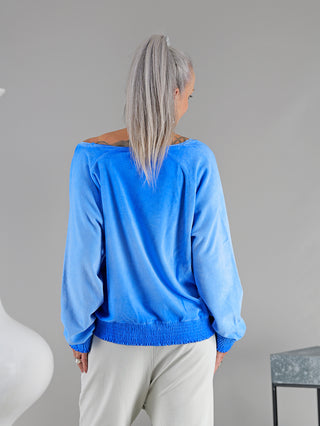 Frau mit langen grauen Haaren trägt das Cotton Candy Sweatshirt Irini newblue, ein lässiges Frottee-Sweatshirt mit V-Ausschnitt und gesmokten Details. Ideal für einen trendigen, vielseitigen Look.