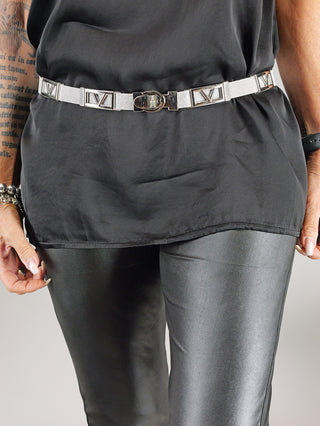 Person trägt den OFF#DLY Gürtel schmal V grey/silver, im Fokus steht die silberne Schnalle. Gürtel aus 70% Metall, 30% Polyester. Sichtbar um Taille, kombiniert mit schwarzem Oberteil.