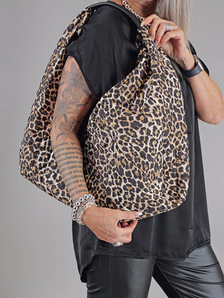 Person mit Tattoos hält den OFF#DLY Leo Shopper, eine große Tasche mit Leopardenmuster. Die Handtasche besteht aus Polyester und misst 55x50 cm.
