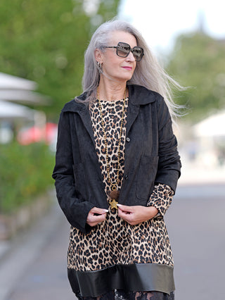 Frau trägt OFF#DLY Jacke Lena black aus Velours Leder Optik, kombiniert mit Sonnenbrille und Leopardenkleid. Jacke hat seitliche Taschen und Knopfleiste.