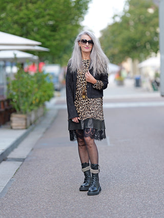 Frau mit langen grauen Haaren trägt die sportliche OFF#DLY Jacke Lena in Velourslederoptik, kombiniert mit einem Leopardenkleid und schwarzen Stiefeln auf dem Gehweg.