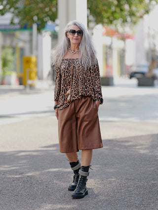 Frau mit langen grauen Haaren trägt Sonnenbrille und Leoparden-Bluse, kombiniert mit den OFF#DLY Short Lilly: stilvolle Fake-Leder-Short mit weitem Bein. Perfekt für trendige Street-Fashion.