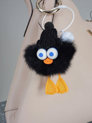 OFF#DLY The Fritz, ein schwarzer, flauschiger Vogel-Schlüsselanhänger mit blauen Augen, gelben Füßen und schwarzem Hut, aus Polyester und Metall gefertigt, perfekt als lustiges Modeaccessoire.