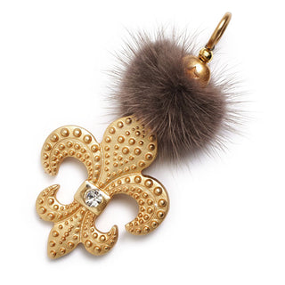 Schautime Lily goldshiny City Amulett: Detailaufnahme eines goldenen, reliefartig verzierten Amuletts mit einem klaren Strass-Stein, ergänzt durch einen flauschigen Fellpuschel und elegante Beads.