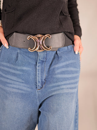 Ein Gürtel CC Groß schwarz mit einer goldfarbenen Schließe, getragen von einer Person in blauen Jeans. Der Gürtel ergänzt perfekt lässige Outfits und ist aus Polyester/Metall gefertigt.