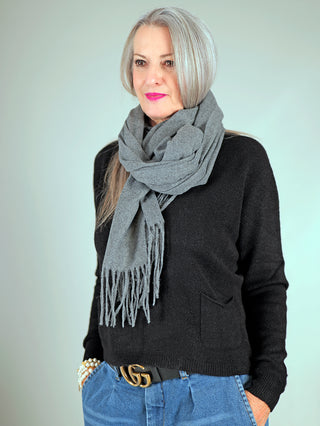 Eine Frau trägt den OFF#DLY Schal Bari midgrey mit Fransen, kombiniert mit einem schwarzen Pullover.