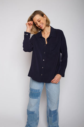 Frau trägt Emily Bluse navy mit überschnittener Schulter und Knopfblende. Die Bluse ist lässig geschnitten und aus weichem Tencel-Material. Sie kombiniert sie mit Jeans.