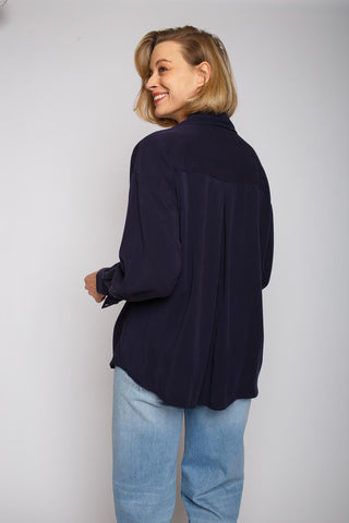 Emily Bluse navy, lässige Oversized-Hemdbluse mit überschnittener Schulter und Knopfblende, getragen von einer lächelnden Frau. Falten im Rückenteil für zusätzlichen Komfort.