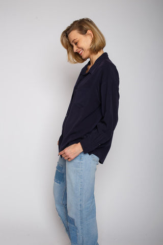 Emily Bluse navy: Frau lächelt in übergroßer Hemdbluse mit überschnittenen Schultern und Knopfblende, aus weichem Tencel, vor weißer Wand. Jeans sichtbar. Model ist 1,68m groß, trägt Größe 36.