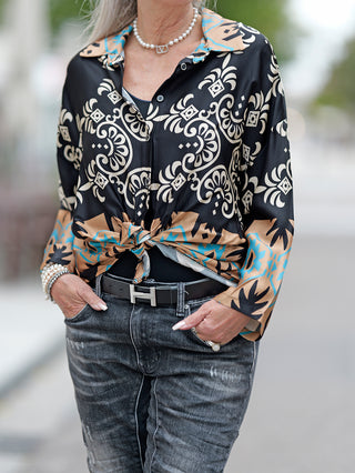Eine Person trägt die OFF#DLY Bluse Rosella mit Printmix und Knopfleiste, während sie die Hände in den Taschen hält. Ein Gürtel und Accessoires ergänzen den Look.