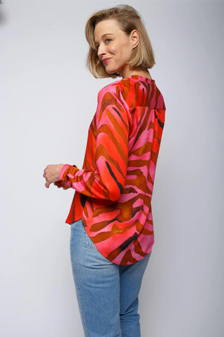 Emily Bluse rot pink zebra, getragen von einer Frau, zeigt einen Stehkragen und halbe Knopfleiste mit langen Ärmeln und schmalen Manschetten im auffälligen Zebra-Print.
