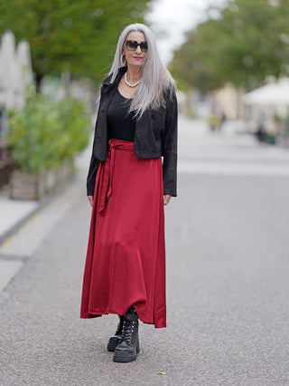 Frau trägt den langen OFF#DLY Rock Camilla burgundy mit Bindegürtel und schwarzer Jacke. Der Rock ist angenehm zu tragen und hat einen Gummizug hinten.