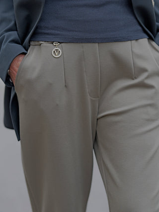 Person trägt OFF#DLY Pant Clara khaki mit Gummibund und seitlichen Taschen, aus Viskose-Nylon-Mix. Nahaufnahme zeigt graue Hose und Hände. Geeignet für Größe 42/44.