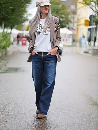 Eine Frau trägt die TAKE 2 Sendai Denim Wide Leg Jeans, eine weite 5-Pocket-Denim in Midblue-Waschung, passend zu ihrer lässigen Street-Fashion mit Jacke und weißen Schuhen.