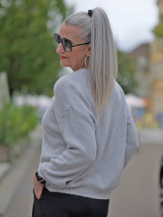 Frau trägt die OFF#DLY Weste Fabiola grey, eine feine kurze Strickjacke mit Knopfleiste und V-Ausschnitt, kombiniert mit Sonnenbrille.
