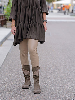 Frau trägt OFF#DLY Fake Leder Legging Frida in taupe, kombiniert mit braunen Stiefeln. Sichtbar ist das enge, lederartige Material, das die Beine der Trägerin betont.