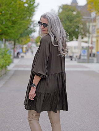 Eine Frau trägt das OFF#DLY Dress Karin, ein kurz geschnittenes A-Linien-Kleid mit V-Ausschnitt, während sie Sonnenbrillen trägt. Ideal für lässige Street-Fashion.