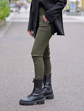 Person trägt OFF#DLY Legging Sonja khaki mit schwarzen Stiefeln. Die Leggings hat seitliche Einschubtaschen und besteht aus Viskose-Baumwoll-Mix. Geeignet für legere Anlässe.