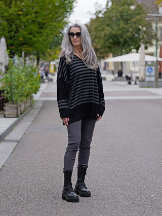 Eine Frau trägt die OFF#DLY Legging Sonja grau auf dem Gehweg, kombiniert mit schwarzen Stiefeln und einem gestreiften Oberteil. Die Leggings hat seitliche Einschubtaschen und sitzt bequem.