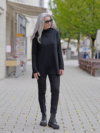 Frau trägt Philomena Pulli WL103 schwarz, einen langen Pulli mit Turtleneck. Kombiniert mit schwarzer Hose und Stiefeln. Ideal für lässige Street-Fashion-Looks.