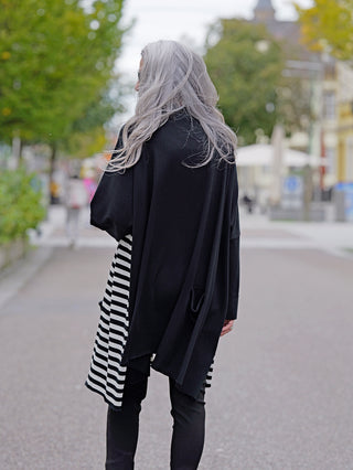 Philomena Jacke Streifen WL226: Frau in langer, schwarz-weiß gestreifter Jacke ohne Knopfleiste, mit seitlichen Taschen, im Straßenmode-Stil.