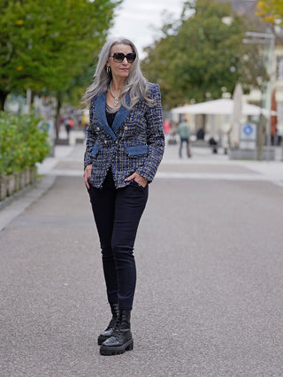 Frau trägt OFF#DLY Legging Sonja dunkelblau mit seitlichen Einschubtaschen, kombiniert mit blauer und weißer Tweed-Jacke und schwarzen Stiefeln, auf der Straße. Perfekt für lässige Street-Fashion.