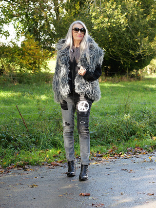 Frau auf Straße in OFF#DLY PEACE Denim; Jeans mit Peace-Symbol auf schwarzem Shirt, Furry-Weste, schwarze Stiefel; leichtes Drehbein, 5-Pocket-Design, getragen in Größe S.