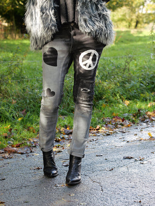 Person trägt OFF#DLY PEACE Denim mit Friedenszeichen und Herzen, kombiniert mit schwarzen Stiefeln. Jeans in Two Color Wash mit leichtem Drehbein und 5-Pocket-Design, perfekt für einen lässigen Look.