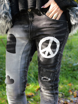 Person trägt OFF#DLY PEACE Denim Jeans mit Peace-Zeichen auf dem Oberschenkel. Die Jeans ist ein Girlfriend-Style mit fünf Taschen und leichtem Drehbein. Materialmix aus Baumwolle, Polyester, und Elastan.