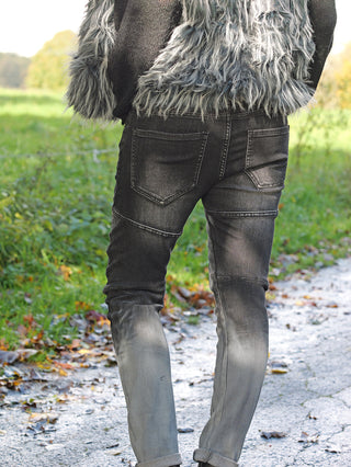 Person trägt OFF#DLY PEACE Denim mit leichtem Drehbein und 5-Pocket-Design, kombiniert mit einem pelzigen Mantel und schwarzen Stiefeln, stehend auf nassem Gras.