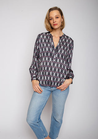 Emily Shirtbluse Fade out black/pink: Frau trägt eine geometrisch gemusterte Shirtbluse mit kleinem Kragen und V-Ausschnitt, kombiniert mit blauen Jeans, lässig posierend.