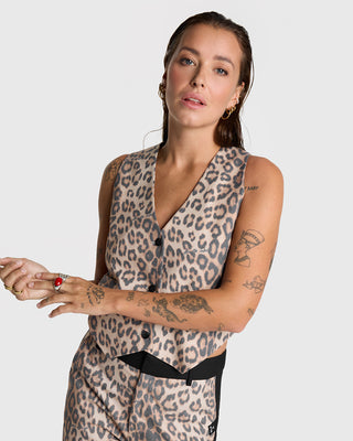 Alix Leo Waistcoat: Frau mit Tattoos trägt ärmellosen, taillierten Gilet mit Leopardenprint. V-Ausschnitt und Knopfverschluss betonen den festlichen Look. Kombinierbar mit passender Hose und Blazer.
