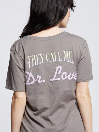 Frau trägt Recycled Karma Kiss Dr. Love T-Shirt mit KISS-Logo und Songtitel auf der Vorderseite. Lockerer Schnitt, weiter Rundhalsausschnitt, abgenutzte Kanten für lässigen Stil.