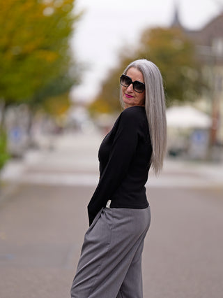 Frau auf Bürgersteig trägt Cotton Candy Ladies Cardigan Lea black, stilvoll mit auffallender Knopfleiste, kombiniert mit grauer Hose und Sonnenbrille, betont modische Eleganz.