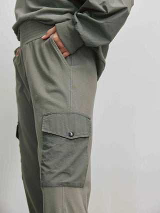 Eine Person trägt die Cotton Candy Ladies Pant Lorna in Olive, eine Sweathose mit seitlichen Taschen, elastischem Bund und geradem Bein.