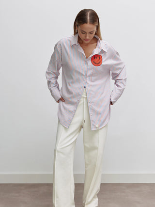 Eine Frau trägt die Cotton Candy Bluse Zoe multicolor mit farbigen Streifen und Knopfleiste, ergänzt durch den Rückenprint ALL YOU NEED ARE GOOD VIBES.