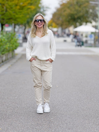 Frau trägt OFF#DLY Cord Pant Ella, eine lässige, gerade geschnittene 5-Pocket-Cordhose, kombiniert mit weißem Pullover und Sonnenbrille, während sie draußen auf der Straße steht.