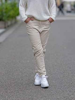Person trägt die OFF#DLY Cord Pant Ella, eine lässige, gerade geschnittene Cordhose mit fünf Taschen. Sichtbare weiße Schuhe und weiße Kleidung ergänzen den Look.