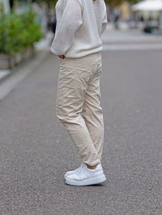 Person trägt die OFF#DLY Cord Pant Ella, eine lässige, gerade geschnittene Cordhose. Sichtbar sind weiße Schuhe und ein weißer Pullover, passend zu den Hosen.