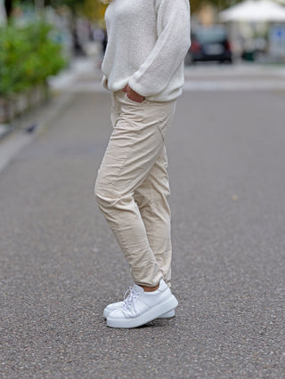 Eine Person trägt die OFF#DLY Cord Pant Ella. Die weiße Hose ist gerade geschnitten und aus Cord. Sichtbar sind auch weiße Schuhe, getragen in einer urbanen Umgebung.